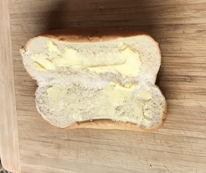 半分に切ったパンにバターを塗った画像