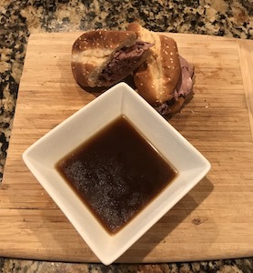 ビーフソースと2つに切ったフレンチディップサンドイッチの画像