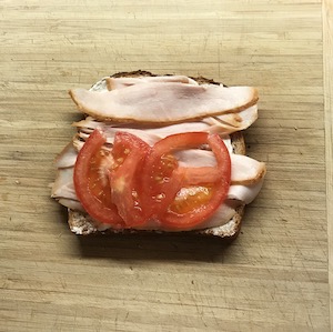 マヨネーズを塗った食パンの上にローストハムとスライストマトを乗せてる画像