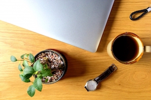 机の上にPCと腕時計とコーヒーと観葉植物を上から写した画像