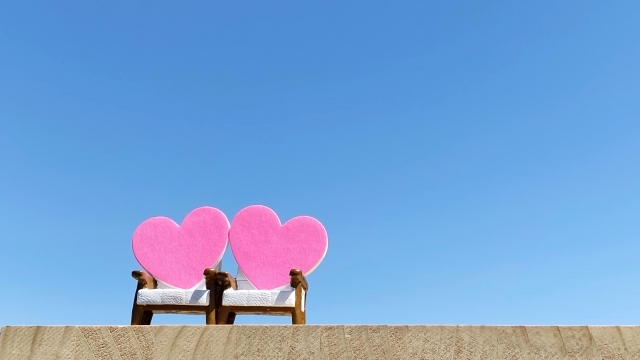 青空の下のベンチにハートの置物が2つ置いてある画像